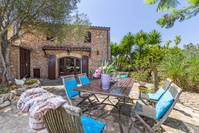 A shaded stone terrace at the finca with a wooden table, blue-cushioned chairs and pink bougainvillea spilling over warm stone walls